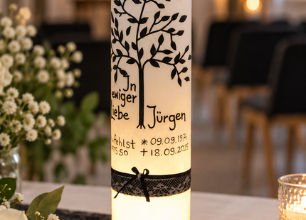 „LED-beleuchtete Trauerkerze mit Lebensbaum und schwarzer Schleife auf einem Gedenktisch mit weißen Blumen.“