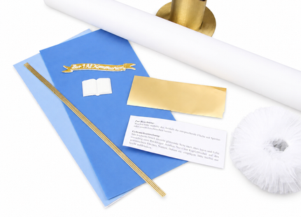 Detailansicht des blau-goldenen Kommunionkerzen Bastelsets mit liegendem Kerzenrohling, goldfarbenem Kerzenständer, blauen Wachsplatten, Goldfolie, Wachsfäden, Echtwachs-Schild, Buchmotiv und Tüll.