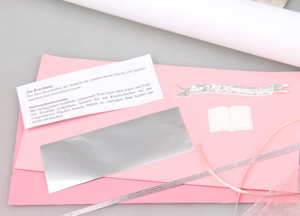 Detailansicht des rosa-silbernen Kommunionkerzen Bastelsets mit rosa Wachsplatten, silberner Schreibfolie, feinen Wachsfäden, Echtwachs-Schild, Buchmotiv, Tüllband, Anleitung und Metallständer.