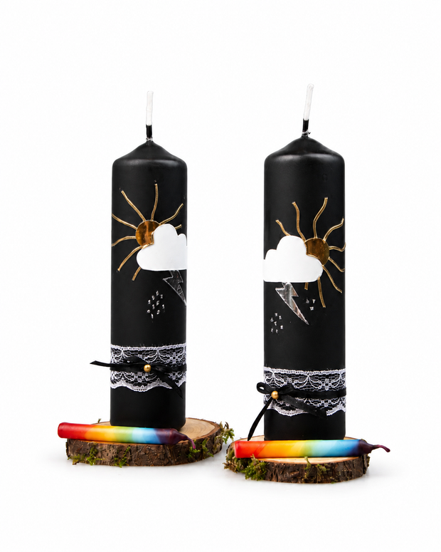 Zwei schwarze handverzierte Gewitterkerzen mit Wolke, Sonne und Blitz auf Birkenholztellern mit Regenbogen-Fidibus.
