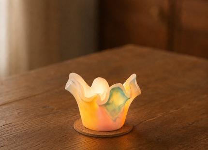 Handgefertigter Lotus-Lichtfang aus Wachs in Aurora-Borealis-Farben, leuchtend auf einem dünnen Korkteller auf Holztisch.