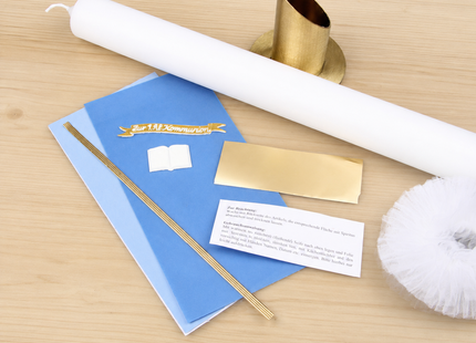 Detailansicht des blau-goldenen Kommunionkerzen Bastelsets mit liegendem Kerzenrohling, goldfarbenem Kerzenständer, blauen Wachsplatten, Goldfolie, Wachsfäden, Echtwachs-Schild, Buchmotiv und Tüll.