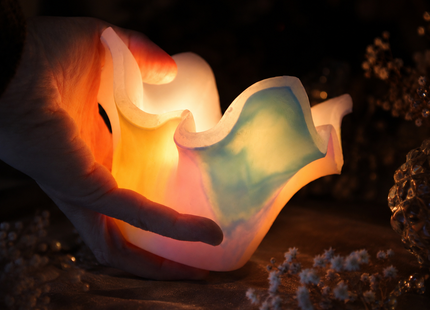 Hand hält einen leuchtenden Lotus-Lichtfang aus Wachs in Aurora-Borealis-Farben mit LED-Licht im Inneren, als Größenvergleich und Seelenlicht.