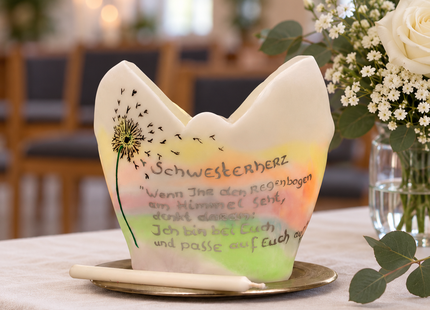 Lichtfang mit Pusteblumenmotiv auf einem Gedenktisch mit weißen Blumen bei einer Trauerfeier.
