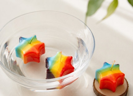 Bunte Sternkerzen im Regenbogen-Design als Schwimmkerzen in einer Glasschale mit Wasser.