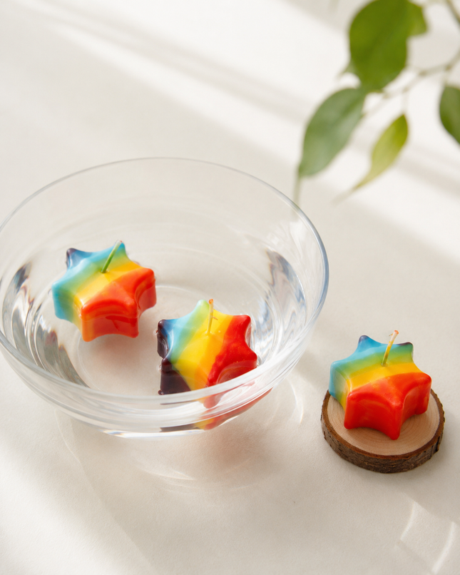 Bunte Sternkerzen im Regenbogen-Design als Schwimmkerzen in einer Glasschale mit Wasser.