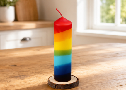 Bunte Regenbogenkerze im Dip-Dye-Style auf Holzscheibe, dekoriert auf einem hellen Holz-Küchentisch bei Tageslicht.