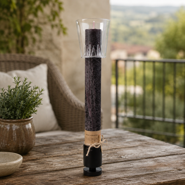 Schwarze Wetterkerze mit transparentem Prozessionsbecher auf einem Holztisch im geschützten Außenbereich