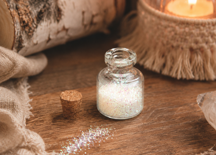 Funkelnder Bio-Glitzer im Glasfläschchen auf rustikalem Holztisch mit Kerzenlicht, Birkenholz und natürlicher Ritualdekoration.