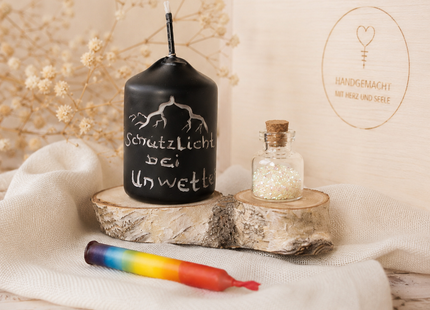 Schwarze Votiv-Wetterkerze mit Blitzmotiv und Schrift Schutzlicht bei Unwetter neben einem Glasfläschchen mit Bio-Glitzer.