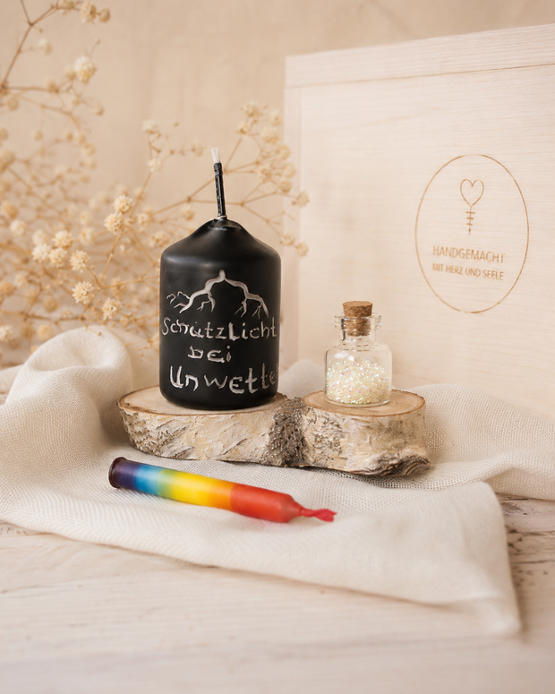 Schwarze Votiv-Wetterkerze mit Blitzmotiv und Schrift Schutzlicht bei Unwetter neben einem Glasfläschchen mit Bio-Glitzer.
